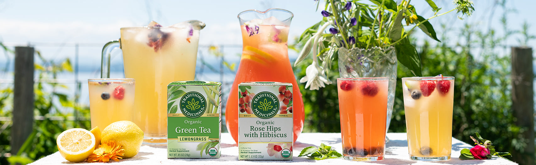 Herbal lemonade in pitchers and glasses with Green Tea Lemongrass and Rose Hips with Hibiscus cartons on table