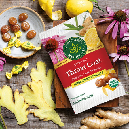Throat Coat® Lemon Echinacea Lozenges package with unwrapped throat drops, lemon, ginger slices and flower next to it.