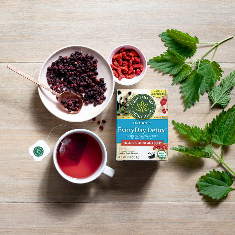Tea, berries, and herbs lay elegantly on a wooden table alongside a box of