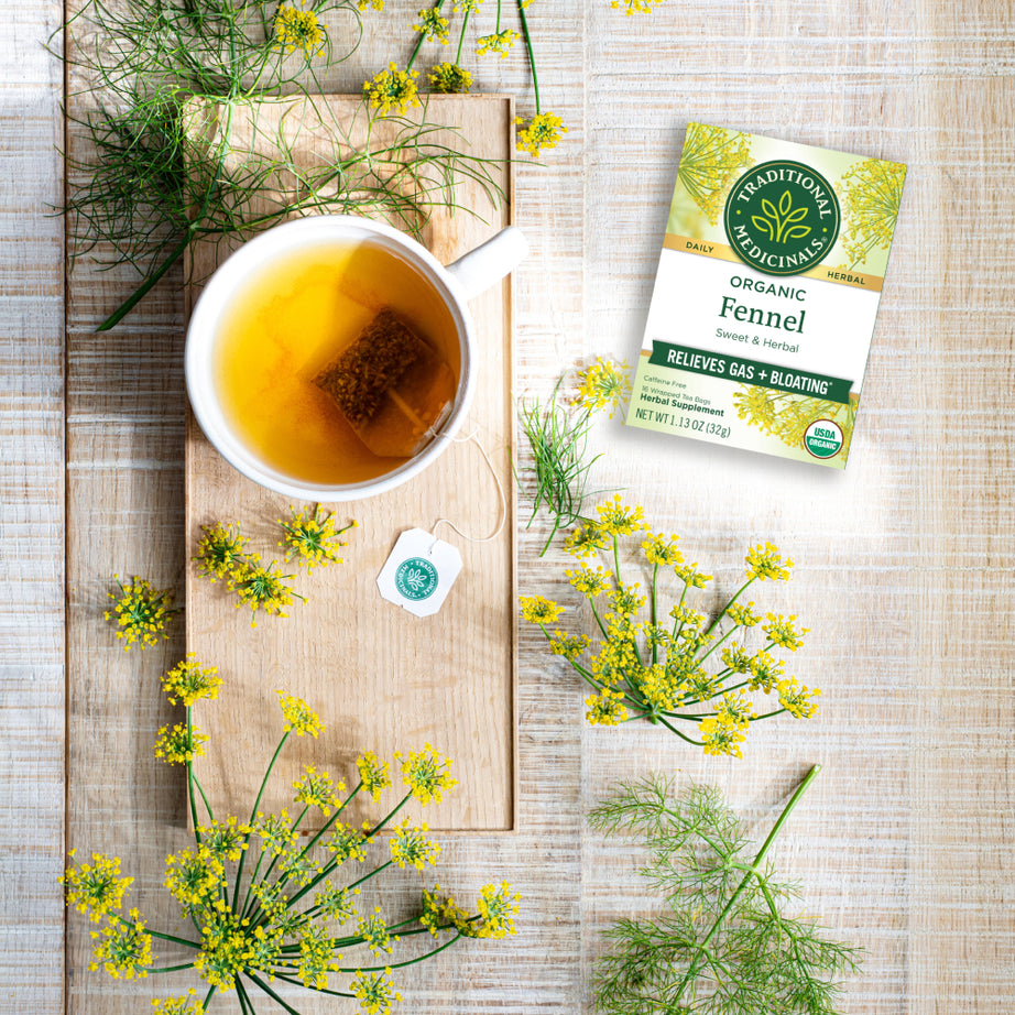 A cup of Fennel Tea rests on a wooden board, surrounded by fresh fennel and its packaging, capturing the spirit of herbalism and enhancing digestive health. View 2