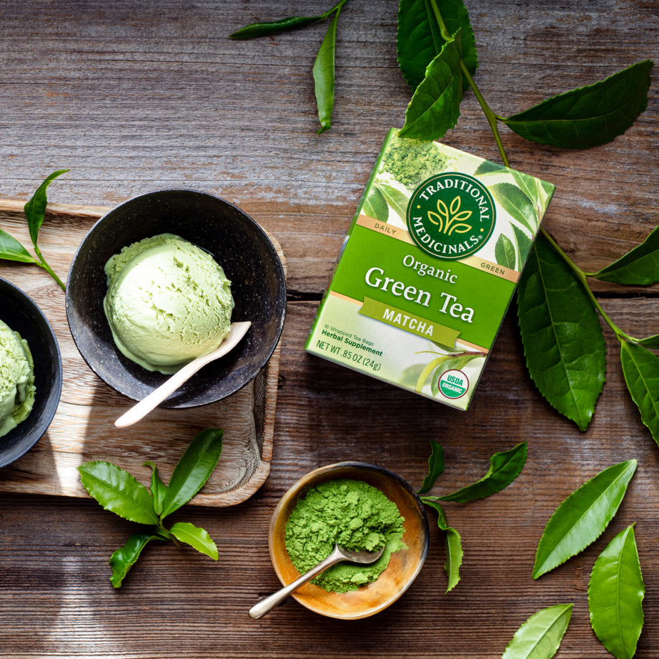 Green Tea Matcha ice cream, a green tea box, and organic Green Tea Matcha powder grace a wooden table adorned with scattered tea leaves, evoking the traditional essence of Japan. View 2