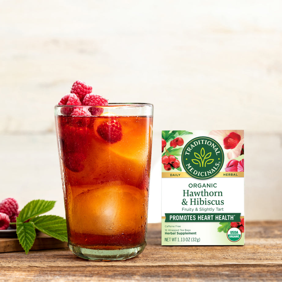 A refreshing glass of iced tea with raspberries sits beside a box of Hawthorn & Hibiscus Tea, combining delightful flavors that support heart health. View 2
