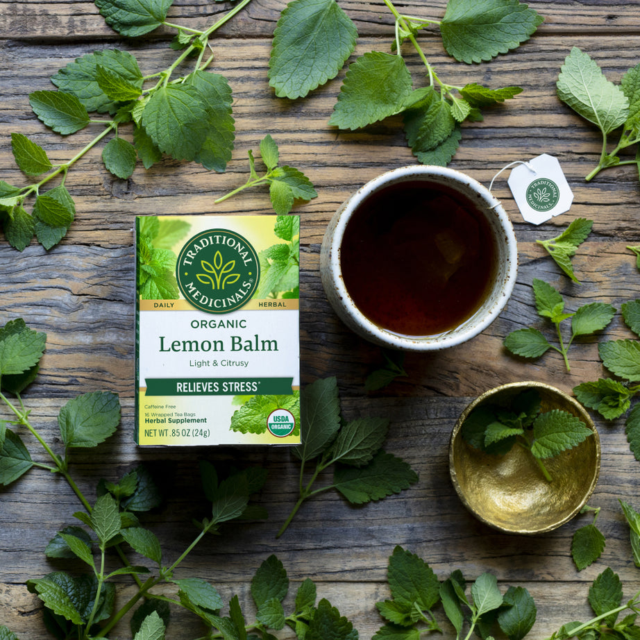 Box of lemon ginger tea alongside a cup and ginger leaves on a wooden surface, perfect for promoting healthy digestion. View 2