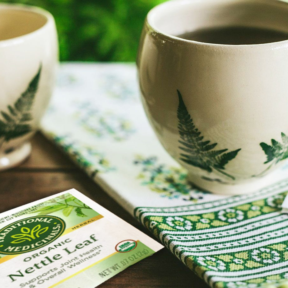 Two cups of herbal tea sit on a patterned cloth next to a package of Nettle Leaf Tea, highlighting its benefits for joint health and overall wellness. View 2