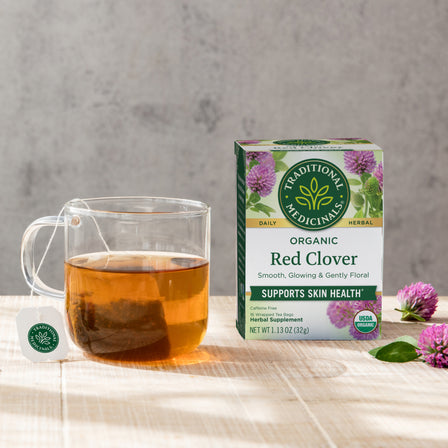 A soothing cup of Red Clover Tea sits beside its box on a wooden table, celebrated in herbal medicine for promoting skin health.