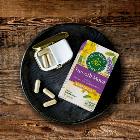 A box and a container of Smooth Move® Capsules rest on a wooden surface, providing natural constipation relief.