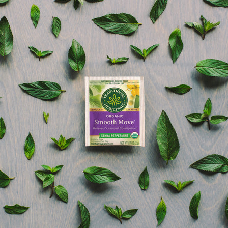 A box of Smooth Move® Peppermint Tea rests among scattered green peppermint leaves, inviting you to sleep easy with its soothing aroma.
