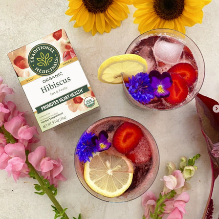 Hibiscus Tea with ice teas, lemon slices, flowers, strawberries in the glass. Flowers around them.