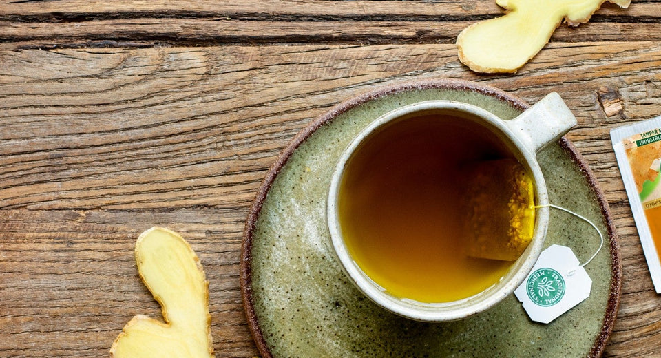 Cup of Ginger Aid tea and tea packets on a table with ginger slices