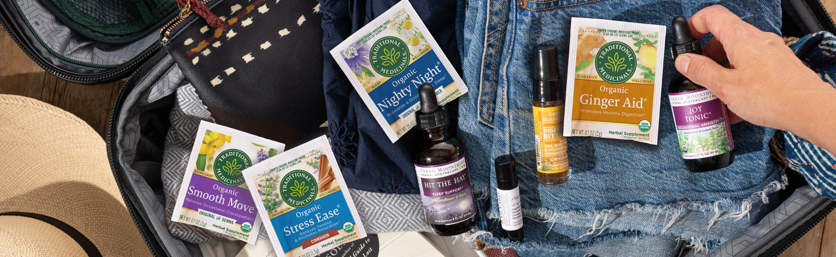 Various Traditional Medicinals tea overwraps and Urban Moonshine tinctures laid out in a suitcase amongst clothing