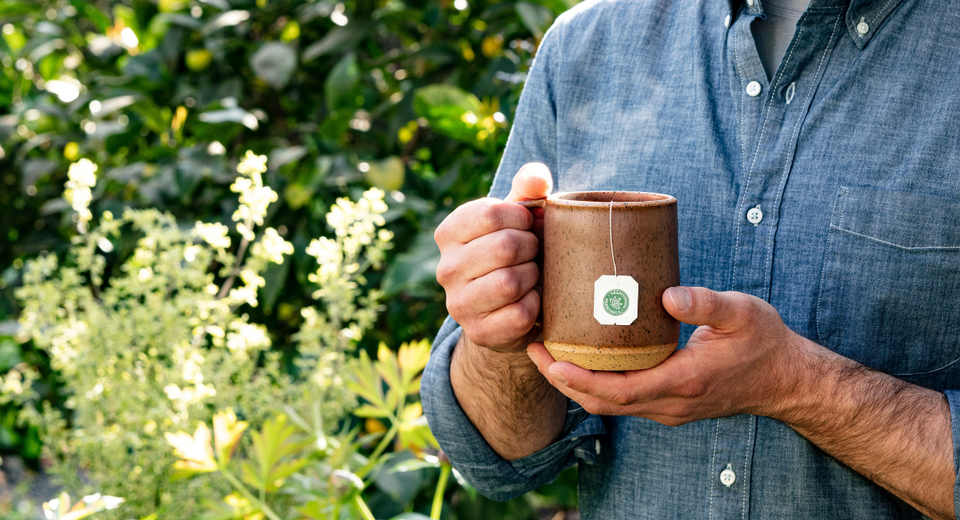 Man holding a cup of tea outdoors with plants behind
