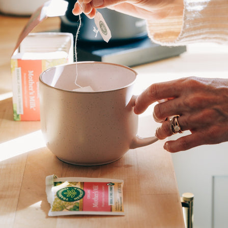 Person making a cup of tea with Mother's Milk tea bags on a wooden table.