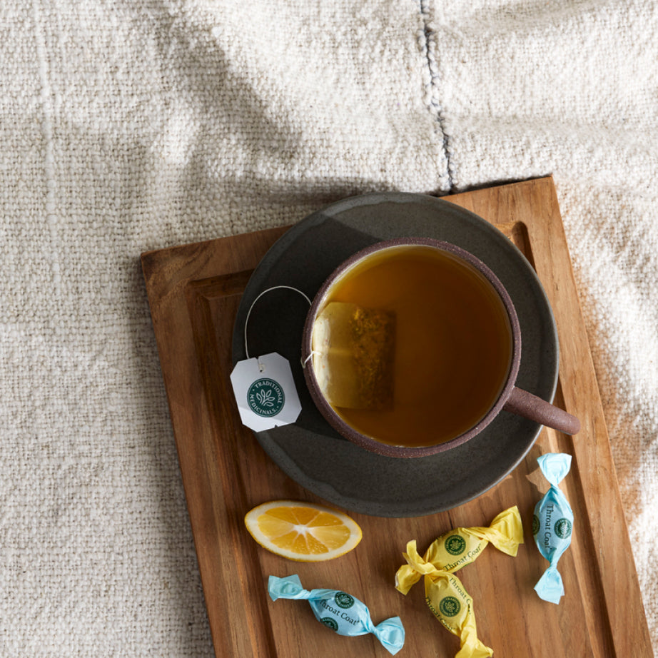 Enjoy a cup of peppermint tea on a wooden tray with a lemon slice and Throat Coat® Eucalyptus Mint Lozenges, 30ct on a textured cloth—perfect for soothing sore throats. View 2