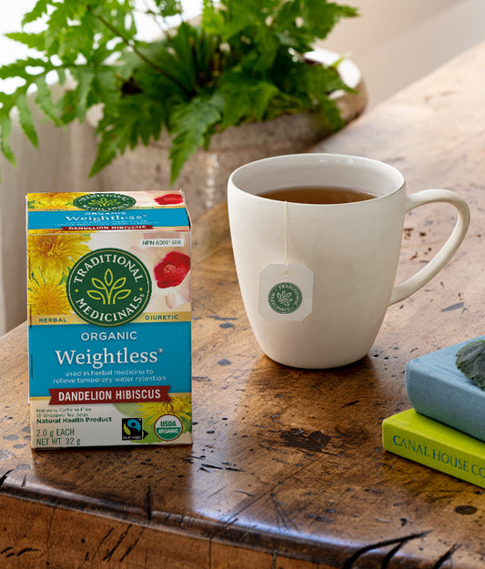 Box of Traditional Medicinals Weightless tea and a cup of tea on a wooden surface with a plant in the background.